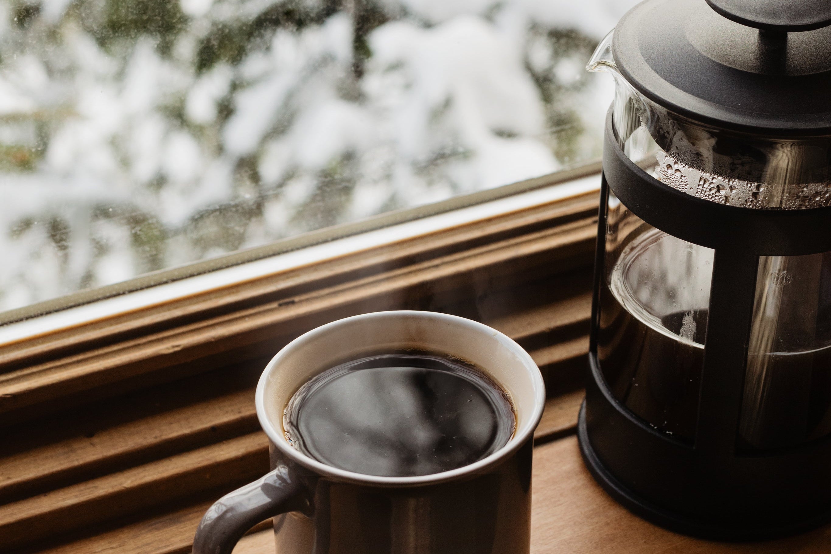 Coffee cup and French press on a windowsill with snow outside