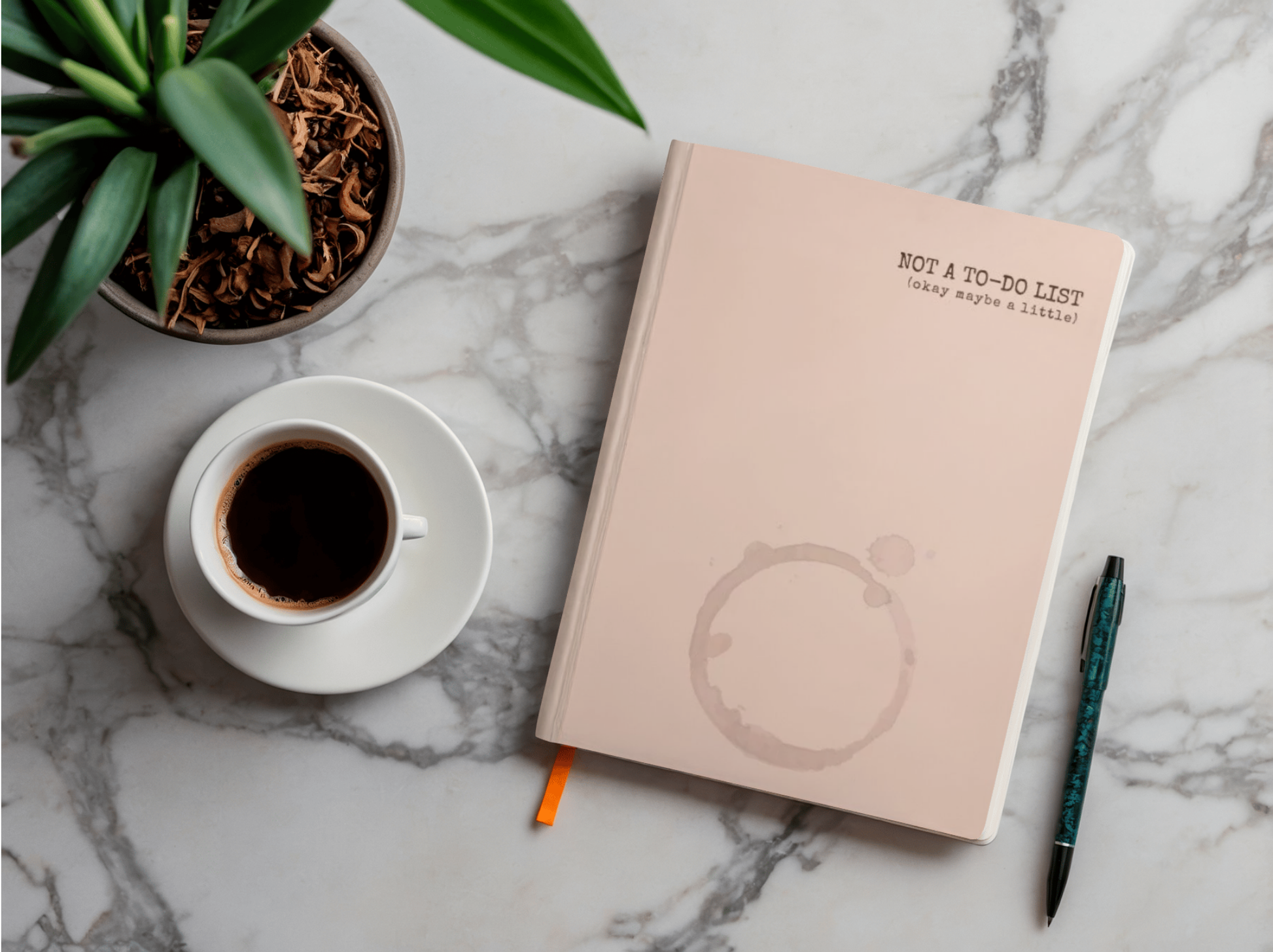 Pink notebook with a plant and coffee cup on a marble surface